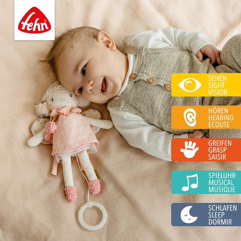 Ein Baby liegt auf einem Bett mit der Mini Spieluhr Fee Plüsch, umgeben von Symbolen und Texten in Deutsch, Englisch und Französisch, die die Funktionen Sehen, Hören, Greifen, Musik (einschließlich Schwanensee) und Einschlafhilfe hervorheben.