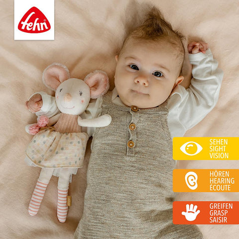 Ein Baby liegt auf einer Decke neben der Bean Bag Maus. Icons betonen die Fähigkeiten Sehen, Hören und Greifen. Das Fehn-Logo, das im Dunkeln leuchtet, ist in der oberen linken Ecke zu sehen.