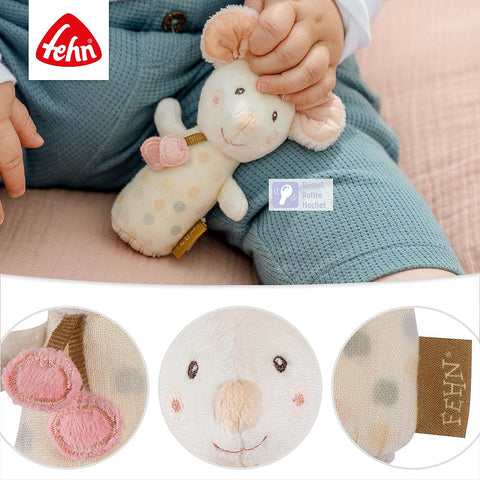 Ein Baby in blauer Hose hält eine Mini-Rassel Maus mit rosa Ohren, einem lächelnden Gesicht und einem braunen Stoffanhänger. Nahaufnahmen zeigen die Ohren, das Gesicht und den Anhänger des Spielzeugs - ideal für die Sinnesförderung.