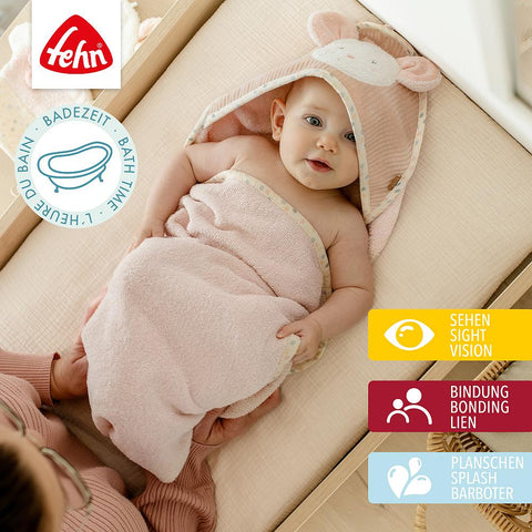 Ein in das rosafarbene Kapuzenbadetuch Maus eingewickeltes Baby liegt auf einer Wickelunterlage und schaut nach oben, während es von jemandem gehalten wird. Text und Icons überlagern das Bild.