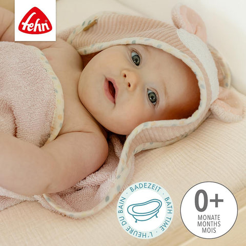 Ein Baby, eingewickelt in das rosa Kapuzenbadetuch Maus mit einer niedlichen Maus-Applikation, liegt auf einer weichen Unterlage. Das Bild zeigt das Fehn-Logo und die Aufschrift, dass es für Kinder ab 0 Monaten geeignet ist.