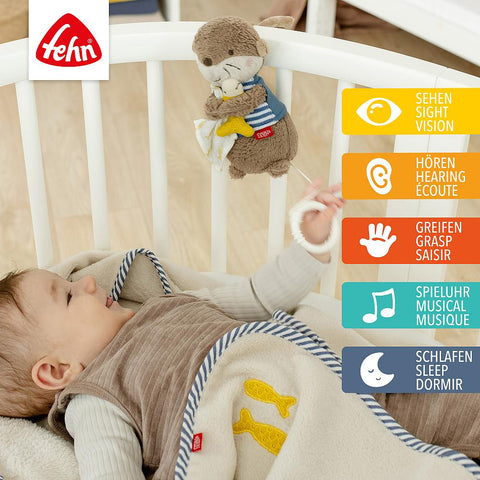 Ein Baby liegt in einem Kinderbett und greift nach der Mini-Spieluhr Otter aus Plüsch. Bunte Etiketten zeigen seine Eigenschaften: Sehen, Hören, Greifen, beruhigende Spieluhr, kuscheliger Otter und Schlafen. Eine Decke deckt das Baby zu.