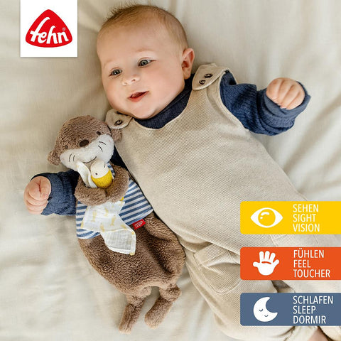 Ein Baby liegt auf einem Bett und kuschelt mit dem Schmusetuch Otter. Oben links erscheint das Fehn-Logo mit drei Symbolen für Kuscheln, Spielen, Trösten - Sehen, Tasten, Schlafen - in Deutsch, Englisch und Spanisch.