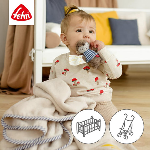 Ein Baby sitzt auf dem Boden und hält ein Stofftier, daneben liegt die Kuscheldecke Otto Otter. Oben links ist das Fehn-Logo zu sehen, unten rechts zwei Spielzeug-Icons - ideal als Geschenk zur Geburt.