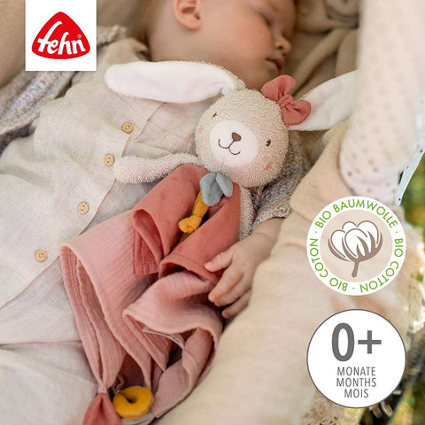 Ein schlafendes Baby kuschelt sich an das Schmusetuch Hase fehnNATUR, ein Fehn-Stofftierhäschen aus Bio-Baumwolle mit rosa Schleife und Decke. Das Bild hebt das Fehn-Branding hervor und weist darauf hin, dass es für 0+ Monate geeignet ist.