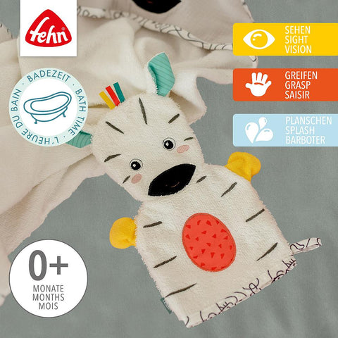 Der Waschhandschuh Zebra, eine Handpuppe in Zebraform aus weichem Frottee, sitzt auf einem Handtuch und ist mit Anhängern zum Sehen, Greifen und Wasserspielen ausgestattet. Geeignet für Babys ab 0 Monaten.