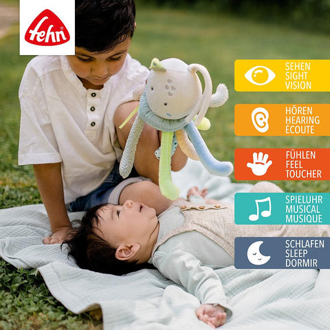 Ein kleiner Junge hält ein Spieluhr-Oktopus-Stofftier über ein Baby, das im Freien auf einer Decke liegt. Daneben sind Symbole für Sinne und Aktivitäten - wie Beruhigende Melodie und Baby-Einschlafhilfe - in Deutsch, Englisch und Französisch abgebildet.