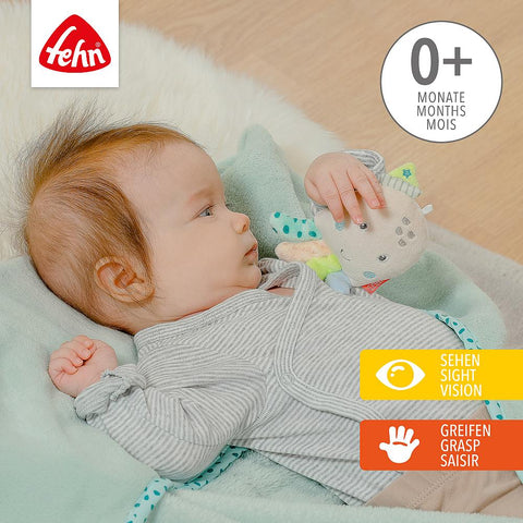 Ein Baby liegt auf der Kuscheldecke Oktopus und hält ein Plüschtier in der Hand. Mit Beschriftungen für 0+ Monate und Symbolen, die die Seh- und Greifentwicklung von Fehn unterstützen, ist es das perfekte Babygeschenk.