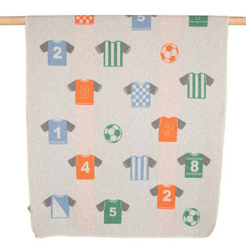 Die JUWEL Kinderdecke Fußball Trikot (100 x 140 cm) zeigt ein leichtes Design mit nummerierten blauen, orangefarbenen und grünen Fußballtrikots sowie passenden Fußbällen - ideal für kleine Fußballfans und aufgehängt an einer Holzstange.