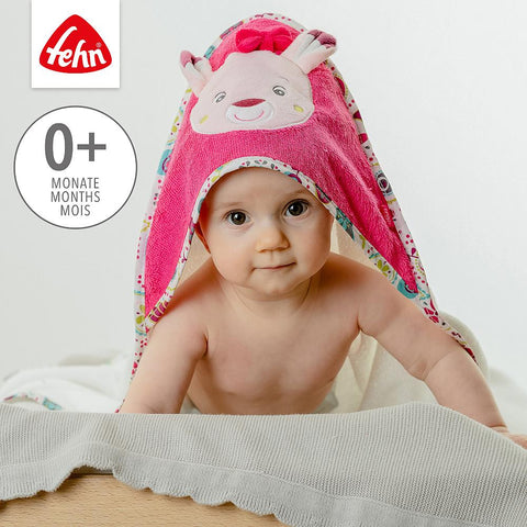Ein Baby sitzt auf einer hellen Fläche und trägt das rosafarbene Kapuzenbadetuch Rehkitz, ein Kapuzenhandtuch mit Rehkitzohren und einem Cartoon-Gesicht auf der Kapuze für einen niedlichen Look.