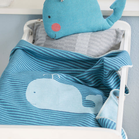 Ein Bettchen mit der JUWEL Decke Wal Streifen, einer blau gestreiften Baby- und Kinderdecke aus Baumwolle mit Walmotiv und einem passenden Wal-Kissen.
