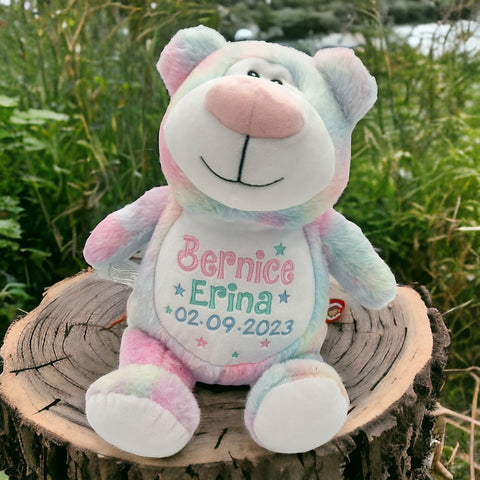 Ein einzigartiger, personalisierter Cubbyford-Bär in zarten Pastellfarben sitzt im Freien auf einem Baumstumpf, mit "Bernice Erina 02.09.2023" auf der Vorderseite bestickt.