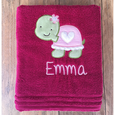 Das Badetuch Calypso Feeling in Cranberry (50x100cm) zeigt eine gestickte grüne Schildkröte, einen rosa Panzer, florale Akzente und kann mit dem Namen Emma personalisiert werden.