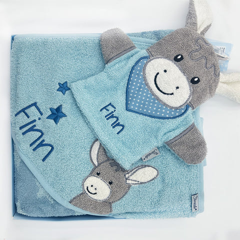 Ein Sterntaler Kapuzenbadetuch Esel Emmi in mittelblau mit Sternchenmuster, bestickt mit dem Namen Finn, und ein passendes Plüschesel-Spielzeug sind wunderschön in einer Geschenkbox präsentiert.
