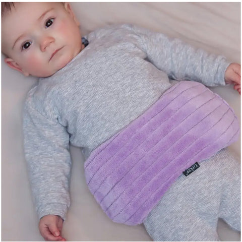 Ein Baby liegt in einem grauen Outfit auf einem Bett, und das KipKep Wärmekissen - Pastellviolett, ein violettes, rechteckiges Kissen, liegt auf seinem Bauch, um es zu beruhigen.