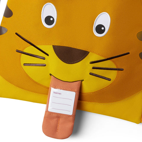 Nahaufnahme des Affenzahn - Turnbeutels - Tiger, einer gelben Sporttasche mit einem Cartoon-Tigergesicht, hergestellt aus recyceltem Polyester. Mit einem Stoffanhänger mit einem Namensetikett, das der Zunge des Tigers ähnelt.