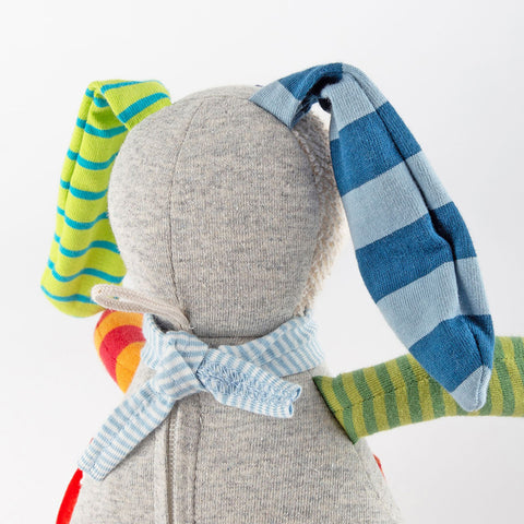 Ein ausgestopfter Hase mit ungleichfarbigen Stoffohren - eine grün-gelb gestreift, eine blau-marine gestreift - und einem blau gestreiften Schal, von hinten gesehen. Die Baby Spieluhr Hase: Ringel Dingel spielt personalisierbare Melodien für Ihr Kind.