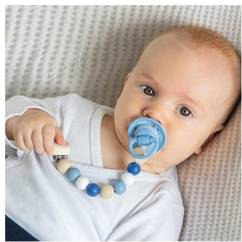 Baby liegt auf einer weichen, strukturierten Oberfläche, trägt ein weißes Hemd, hält die Schnullerkette Stern, blau-perfekt als liebevolles Babygeschenk.