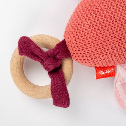 Ein Holzring mit kastanienbraunem Stoffknoten steht neben dem Strick-Greifling Schmetterling - 20 cm, einem rosa Strickschmetterling von sigikid mit rotem Etikett.