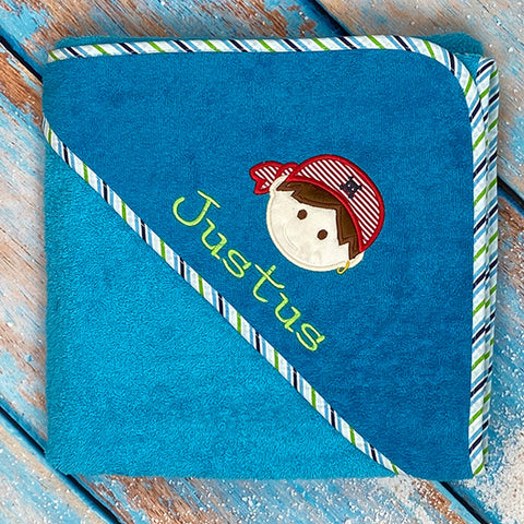 Das Kapuzenbadetuch Aqua/Petrol 100x100cm besteht aus weichem Frottee, ist gestreift und wird mit dem Namen Justus sowie einem Cartoon-Kind mit rot-gestreiftem Piratenhut personalisiert.