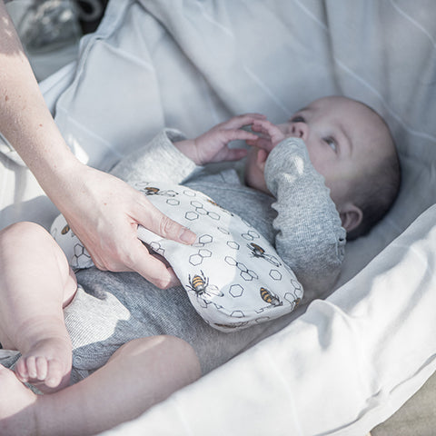 Ein Baby im Kinderwagen trägt ein graues Outfit, während ein Erwachsener das KipKep Wärmekissen - ECO Biene Special auf die Brust des Babys legt, um Koliken zu lindern.