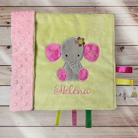 Gelb-rosa Schmusedecke mit pinkem Elefanten und dem Namen ‚Helena‘, mit bunten Stoffbändchen.