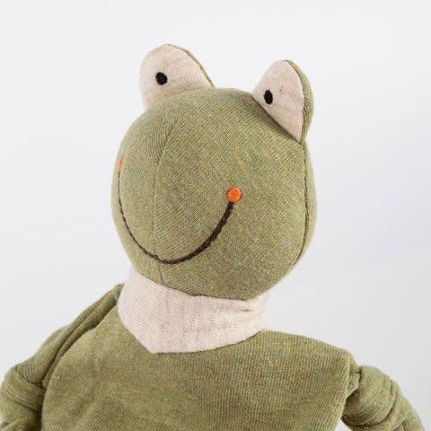 Eine Nahaufnahme des Mini Jersey Schnuffeltuch Frosch, ein grüner Plüschfrosch aus Mini Bio-Baumwolljersey, mit gestickten Augen, einer orangen Nase und einem großen braunen Lächeln. Ideal für die sensorische Entwicklung.