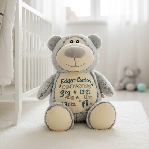 Ein Cubbyford, grauer Bär mit beigen Akzenten sitzt im Kinderzimmer. Auf seinem Bauch sind Geburtsdaten und Fußabdrücke des Babys aufgestickt - ein perfektes personalisiertes Plüschtier Geschenk für Kinder.