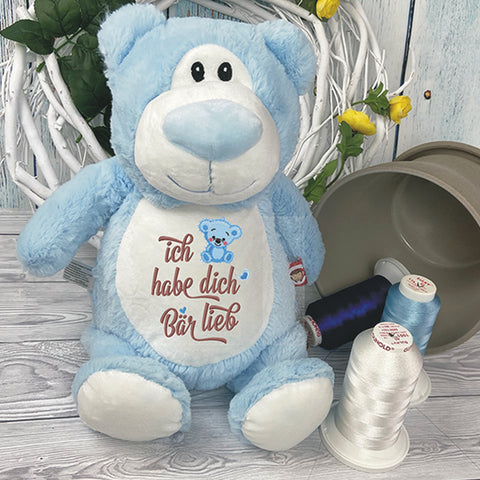 Der "Blauer Bär - Cubbyford" mit "Ich habe dich Bär Lieb"-Stickerei sitzt neben weißen und blauen Garnspulen und einem gelben Blumenkranz - ein maschinenwaschbares Geschenk für jeden Anlass.